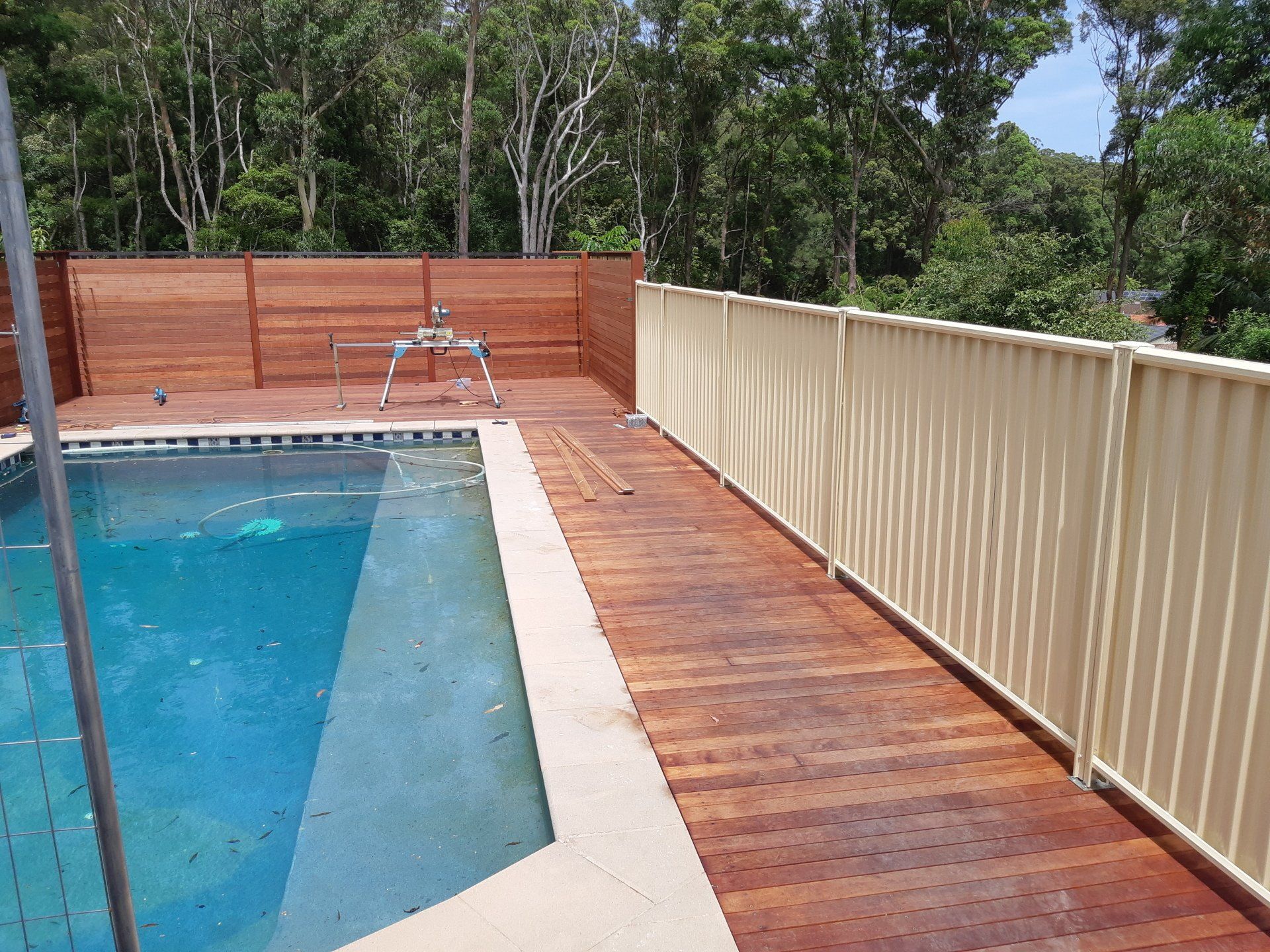 A Fence Surrounds A Swimming Pool With A Wooden Deck — Boambee Home Improvements in Coffs Harbour, NSW