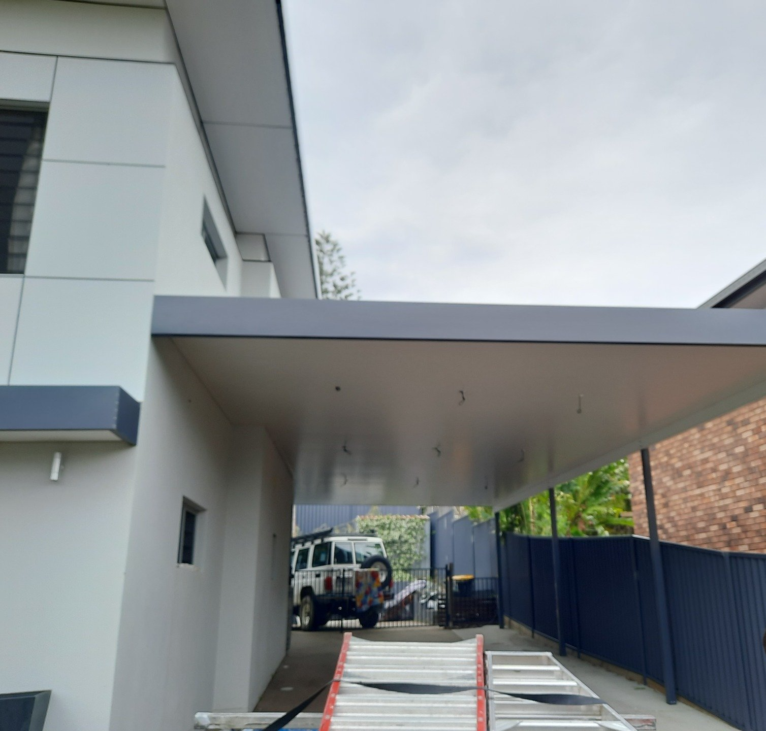 A White Car Is Parked Under A Canopy Next To A Ladder — Boambee Home Improvements in Coffs Harbour, NSW