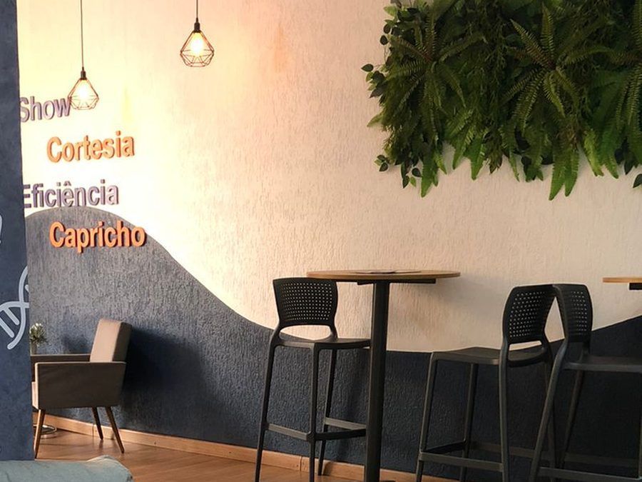 Espaço de convivência do polo do Instituto Focar, com mesas altas, luminárias pendentes e jardim vertical