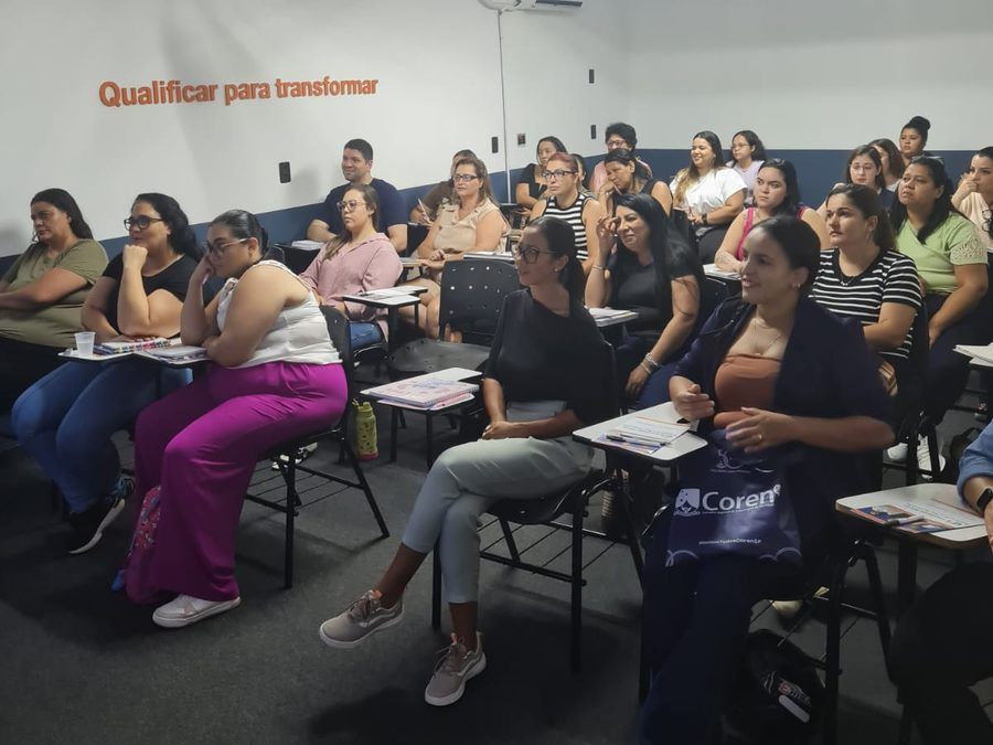 Turma presencial sorrindo em sala de aula do Instituto Focar, com o lema Qualificar para transformar na parede