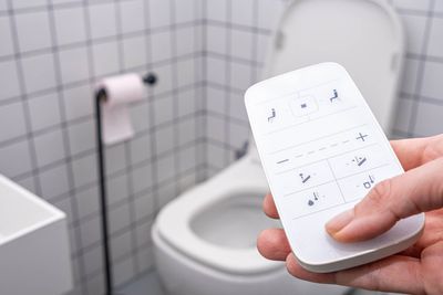 a person is holding a remote control in a bathroom in front of a toilet.
