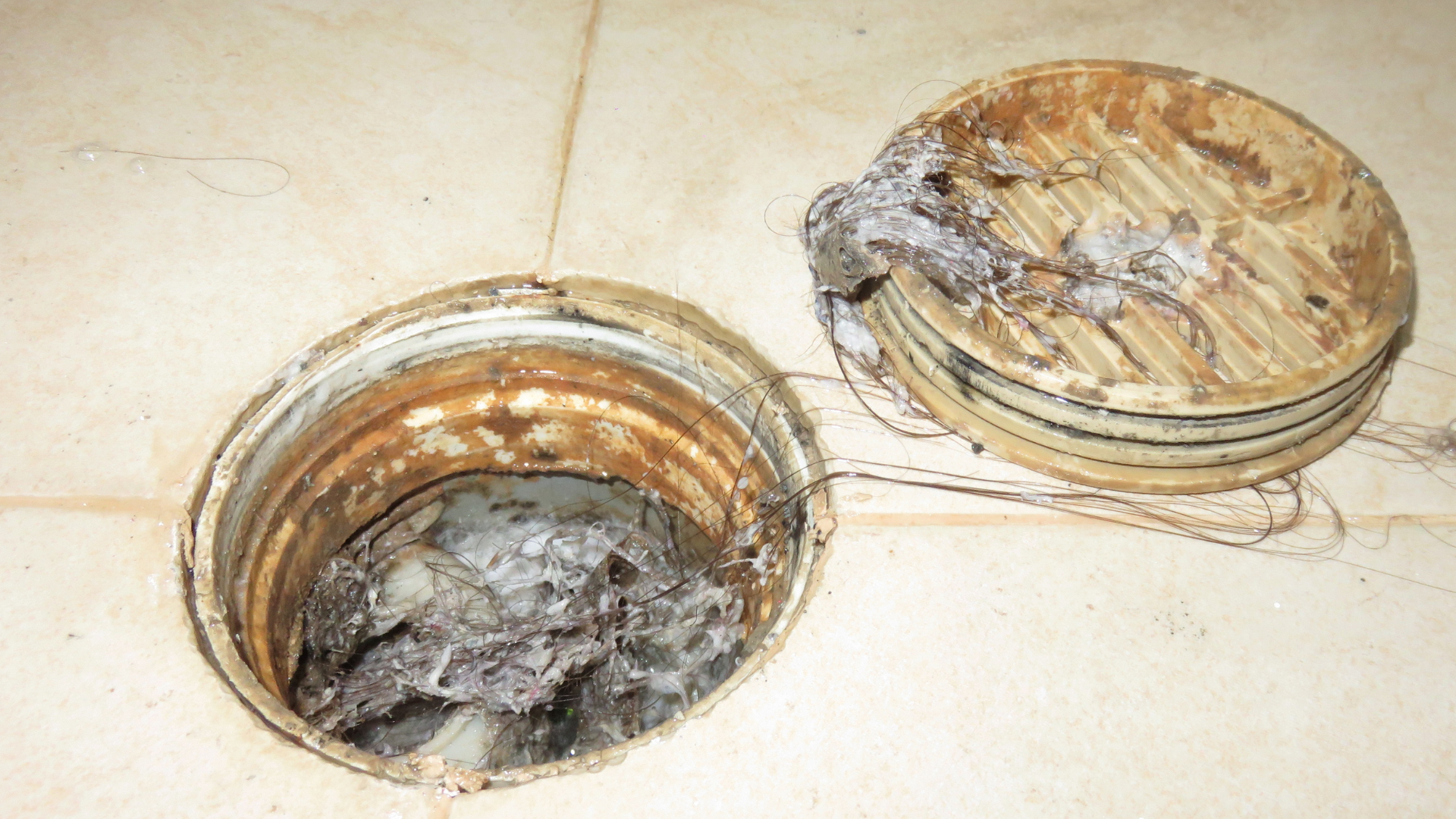 two drains on a tiled floor with one filled with dirty water .