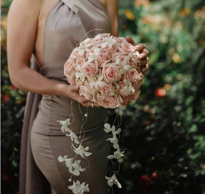 Una persona tiene in mano un bouquet di rose rosa pallido con ricadenti di verde durante un matrimonio all'aperto.