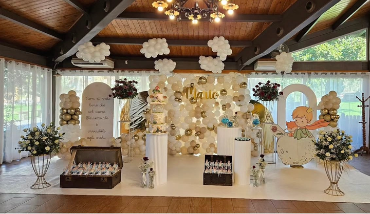 Elegante tavolo da dessert al coperto con decorazioni floreali dorate e bianche, torte e ornamenti di carta appesi.