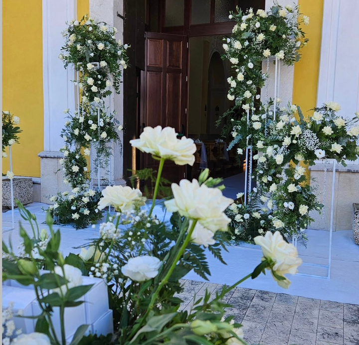 Fiori bianchi incorniciano un ingresso con pareti gialle e una porta di legno scuro.