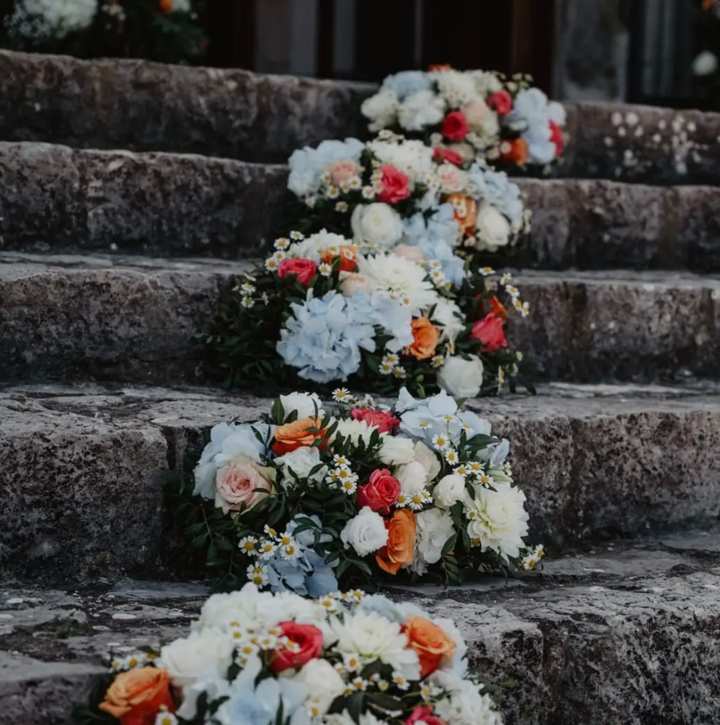 Composizioni floreali bianche e rosse posizionate su gradini di pietra all'aperto