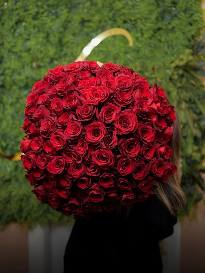 Una persona tiene un grande mazzo di rose rosse sulla spalla, davanti a una distesa di verde.