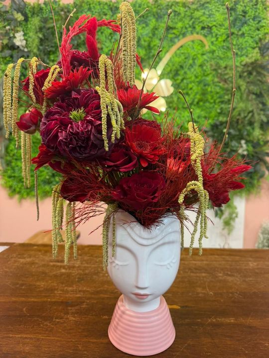 Composizione floreale rossa e verde in un vaso bianco su un tavolo di legno.