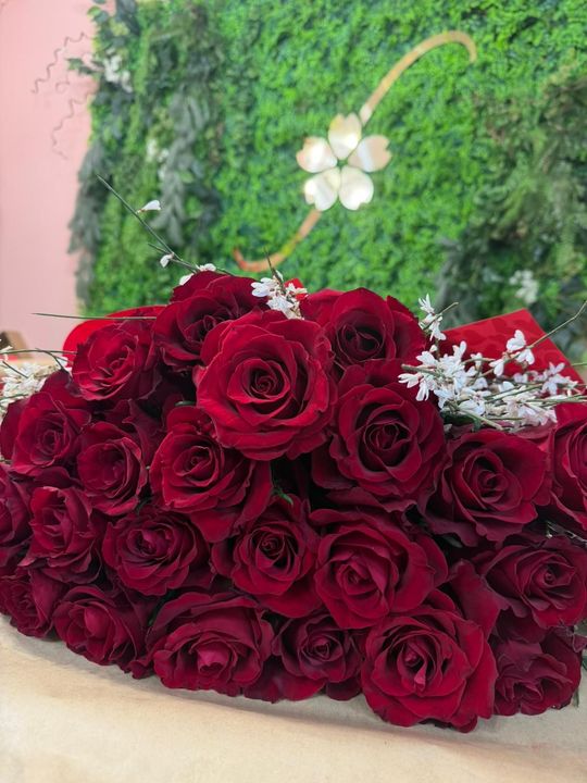 Bouquet di rose rosse con piccoli fiori bianchi su sfondo verde.