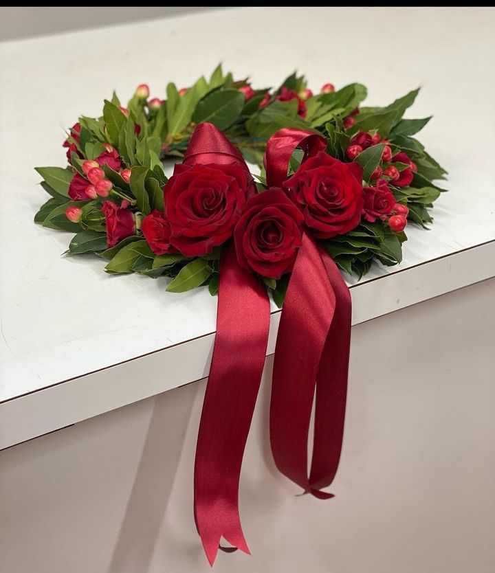 Bouquet di rose rosse con foglie verdi e lunghi nastri rossi su uno sfondo bianco.