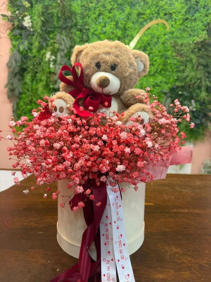 Orsacchiotto con nastro rosso in un bouquet di gypsophila rosa su un supporto bianco