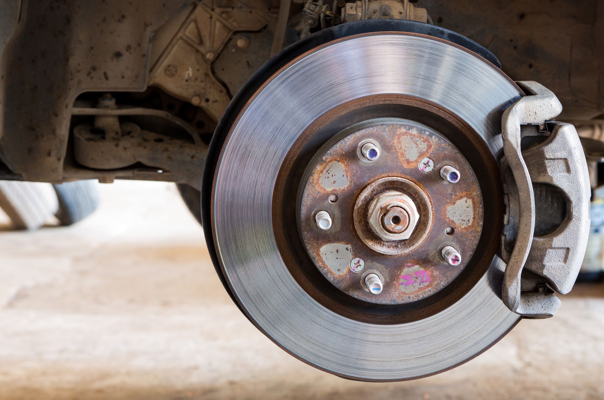 Car wheel with exposed brake disc and caliper, showing rust and wear.
