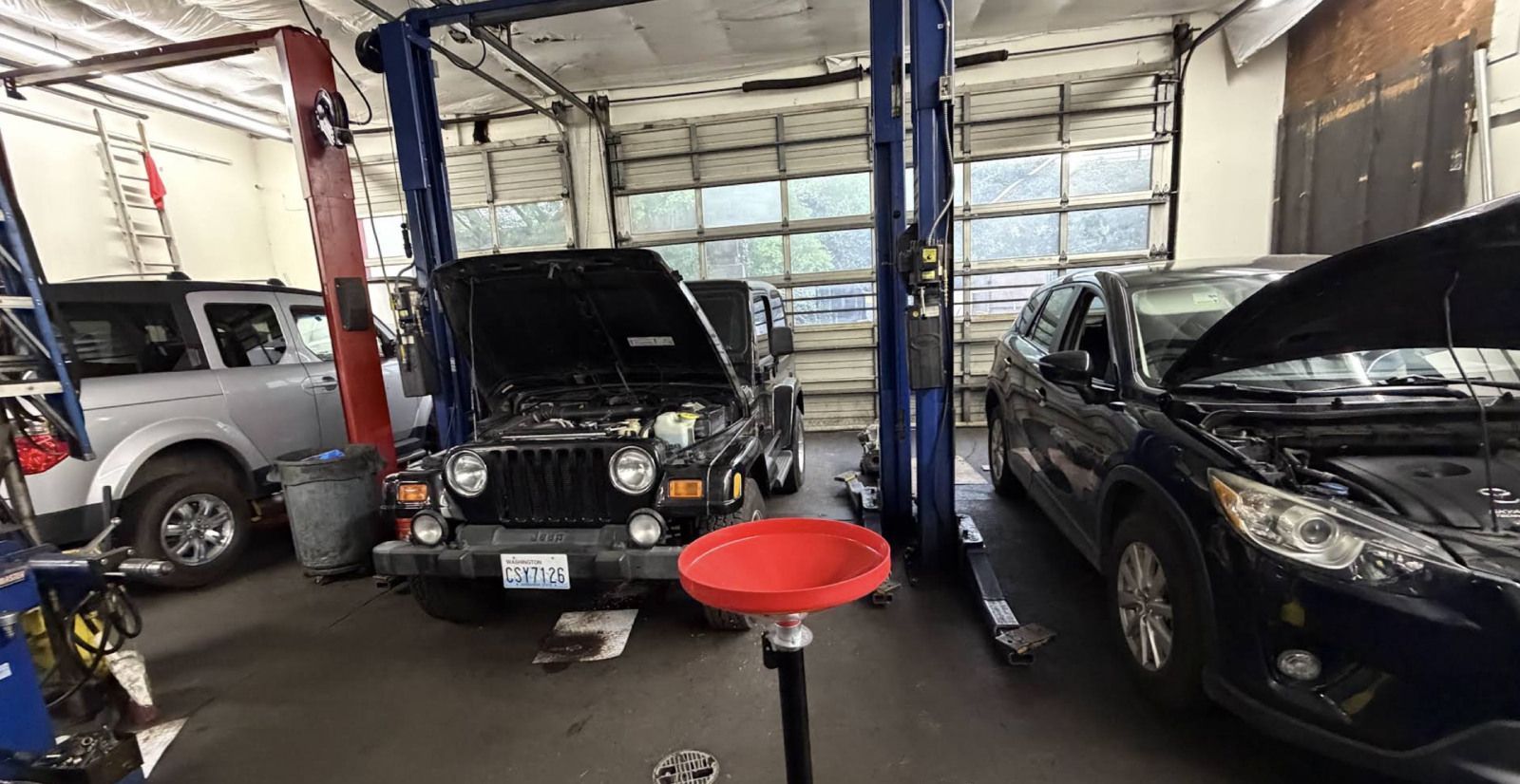 Auto repair shop with several cars, including one on a lift and another with its hood open.