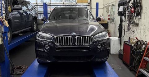 Black SUV on a service lift in an auto repair shop, viewed from the front.