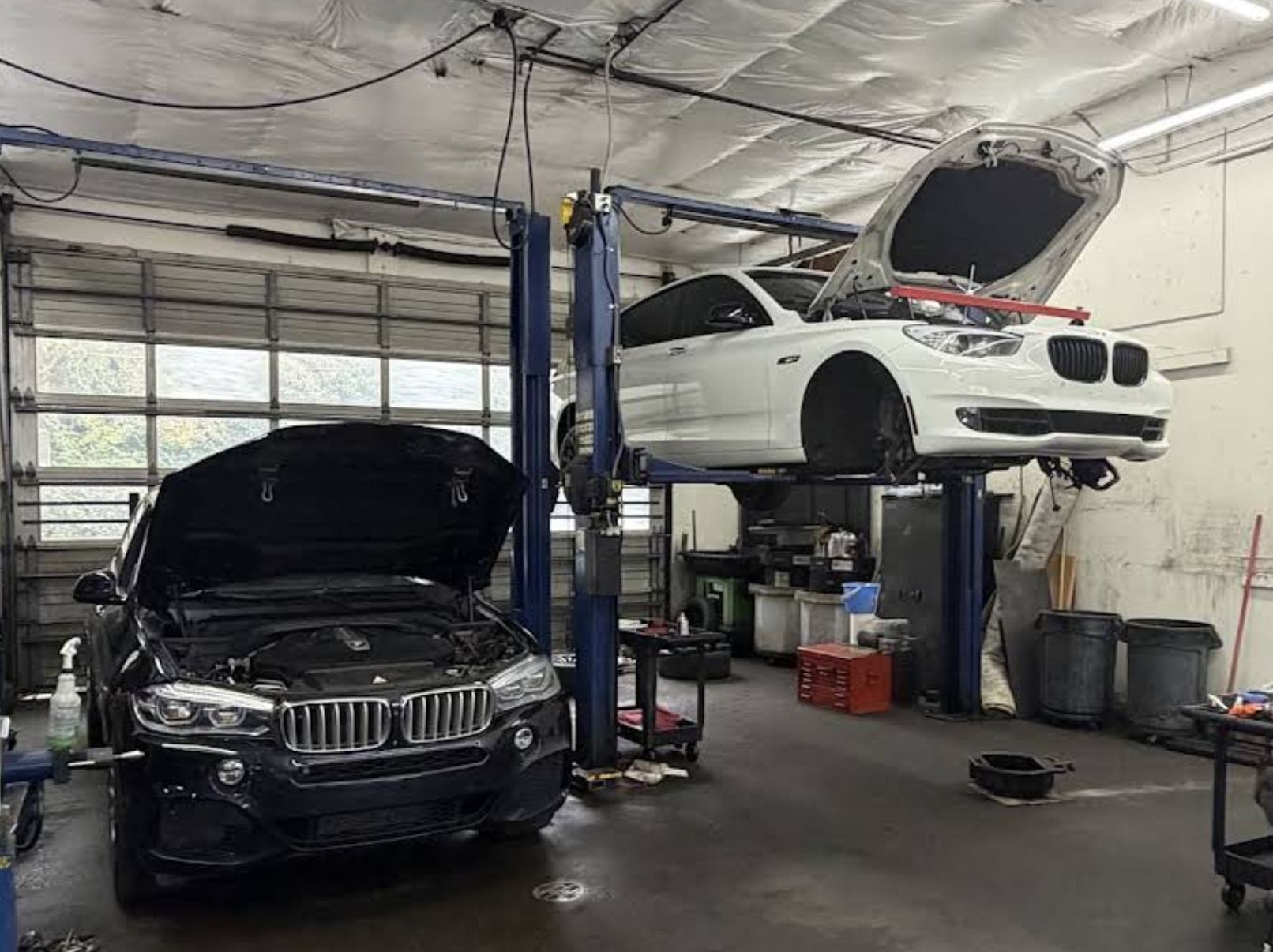 Auto repair shop with a black car below a white car raised on a lift