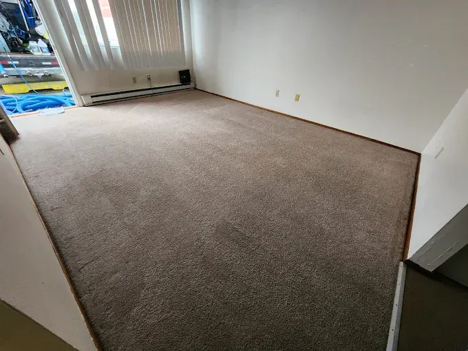 Empty room with brown carpet, white walls, and a window with blinds.