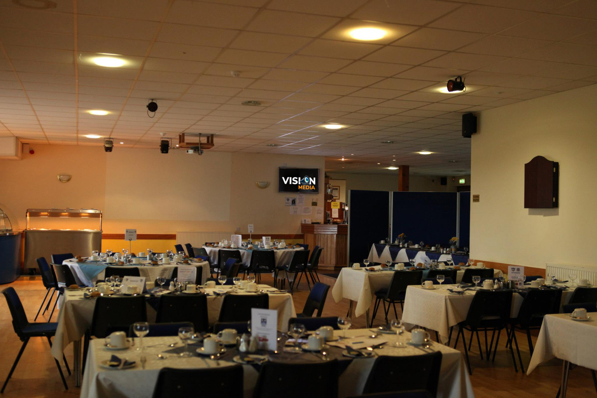 Empty banquet hall with round tables, white tablecloths, and dim ceiling lights
