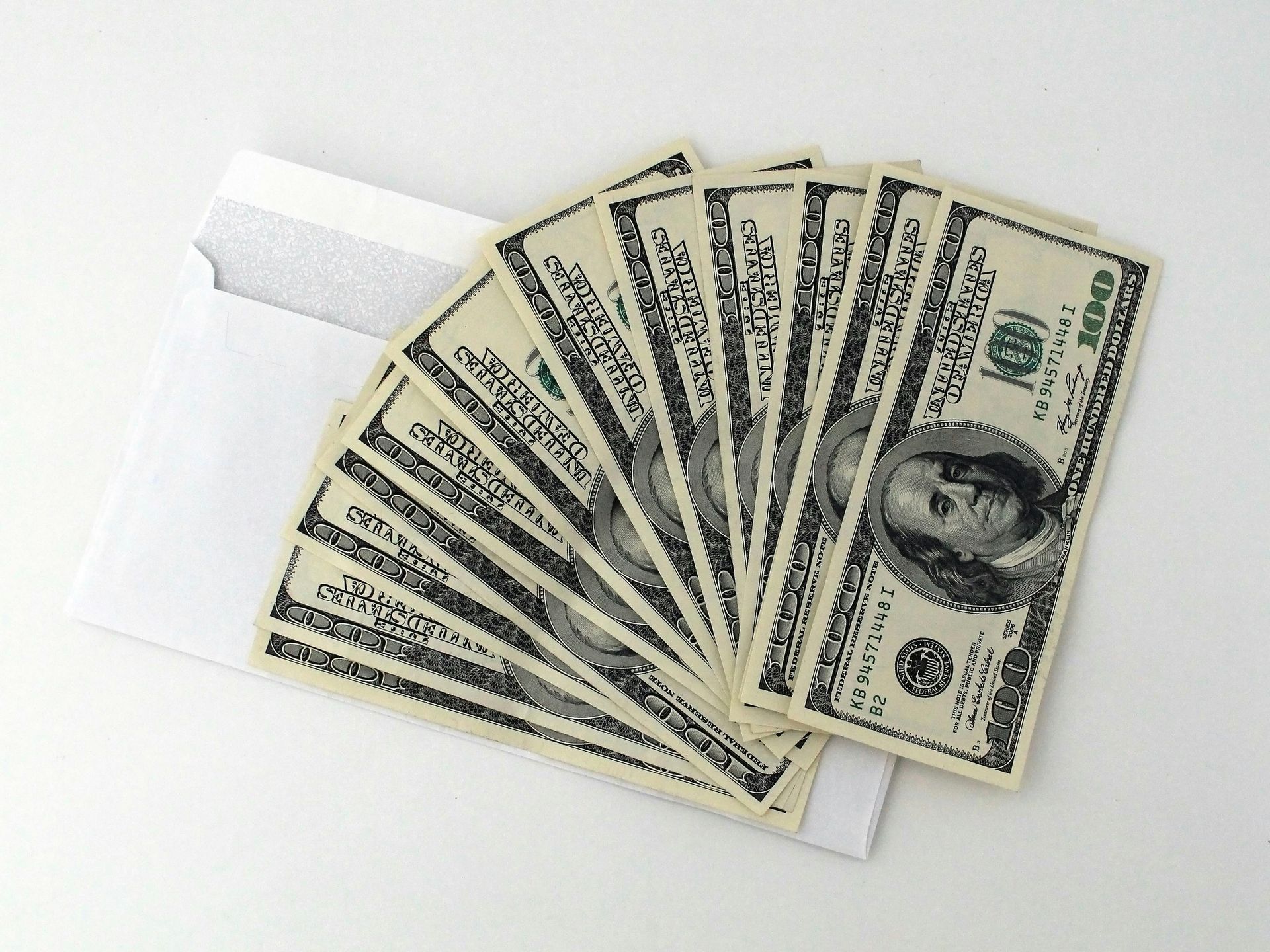 Fan of hundred dollar bills emerging from a white envelope.
