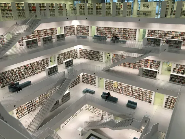 Multi-level library interior with white walls, bookshelves, stairs, and people reading.