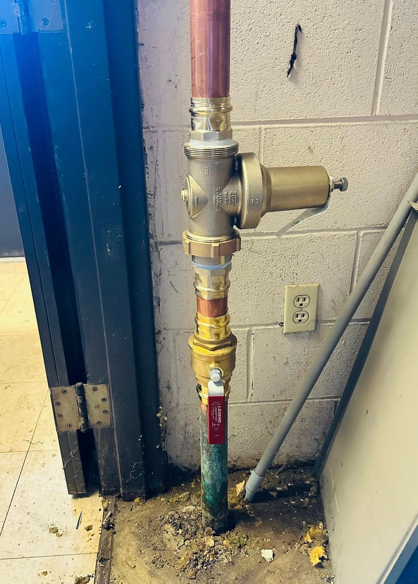 A copper pipe with a valve on it is sitting next to a brick wall.
