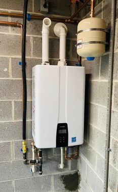 A white water heater is hanging on a wall next to pipes.