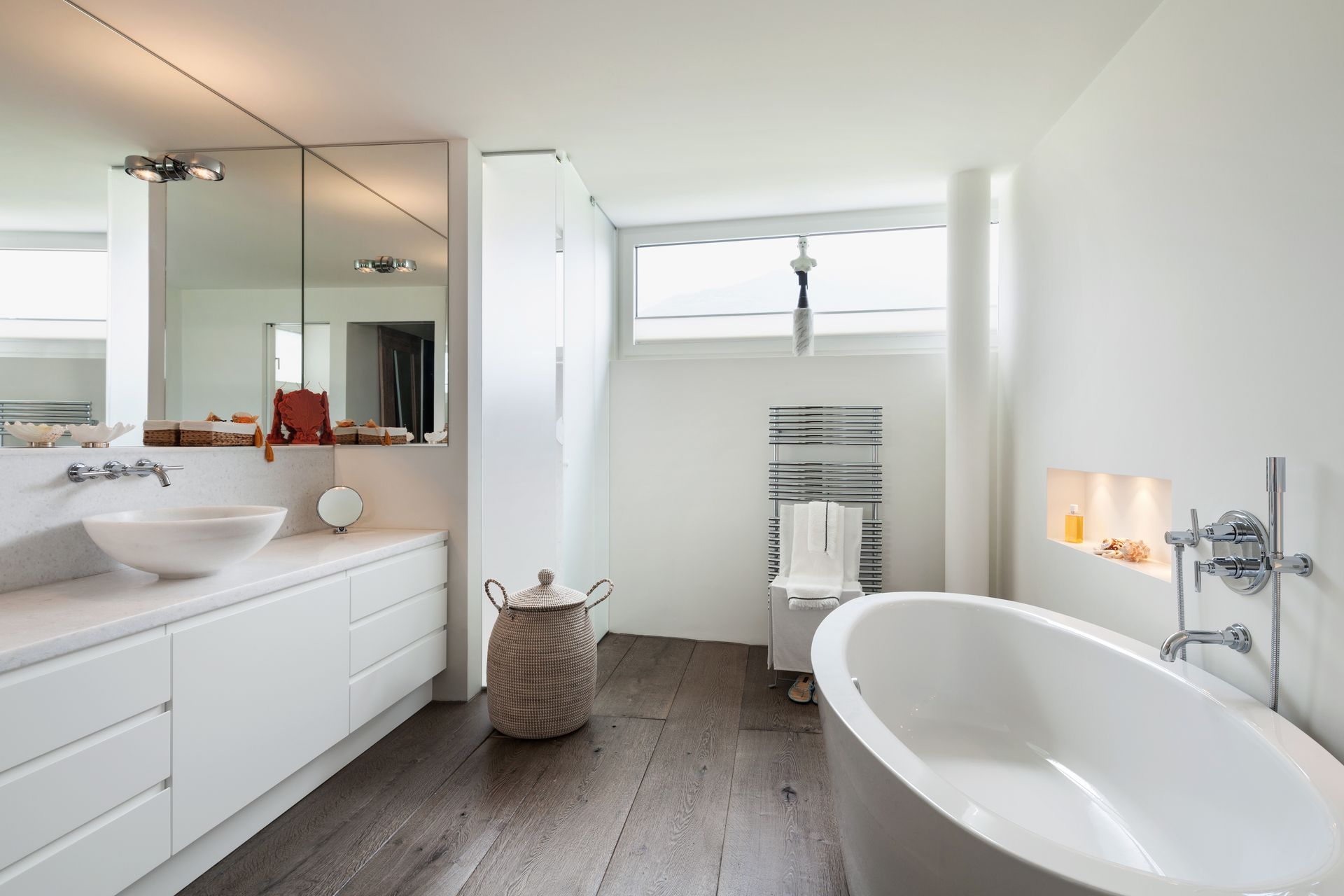 Modern bathroom with a white oval tub, wooden floors, a floating vanity with a vessel sink, and a mirrored wall. Modern bathroom with a white oval tub, wooden floors, a floating vanity with a vessel sink, and a mirrored wall.