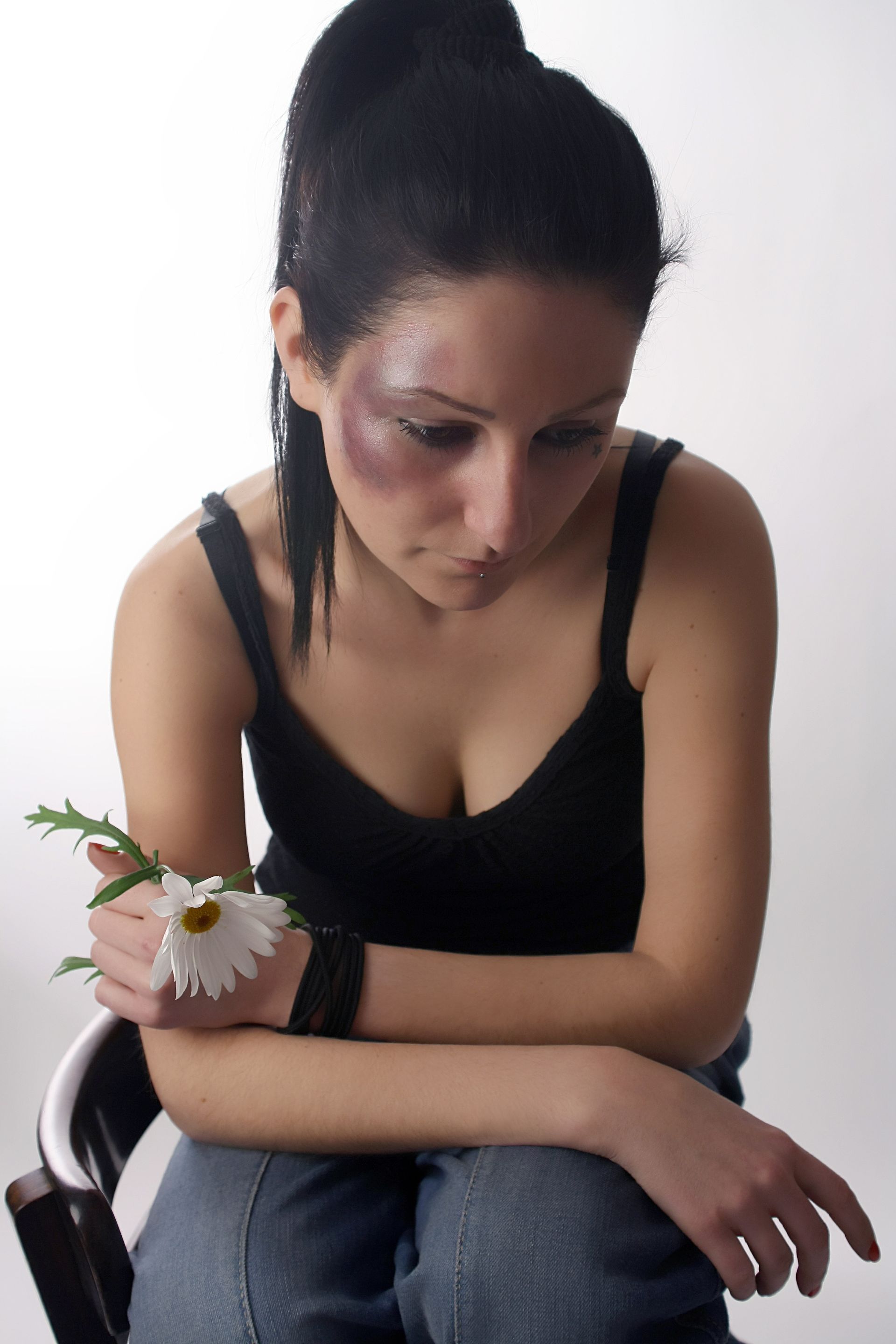 A woman sitting and holding a white daisy flower.