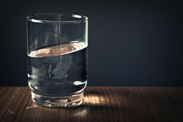 Glass of water, half full, on a wooden surface with a dark background.