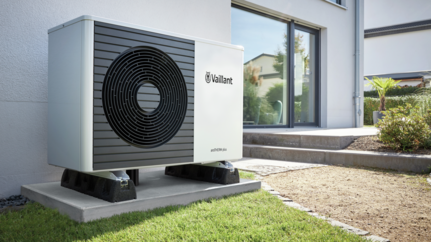 Un'unità esterna per pompa di calore Vaillant, di colore bianco e grigio, montata su una base di cemento accanto a una casa moderna Mattei Vaillant Roma