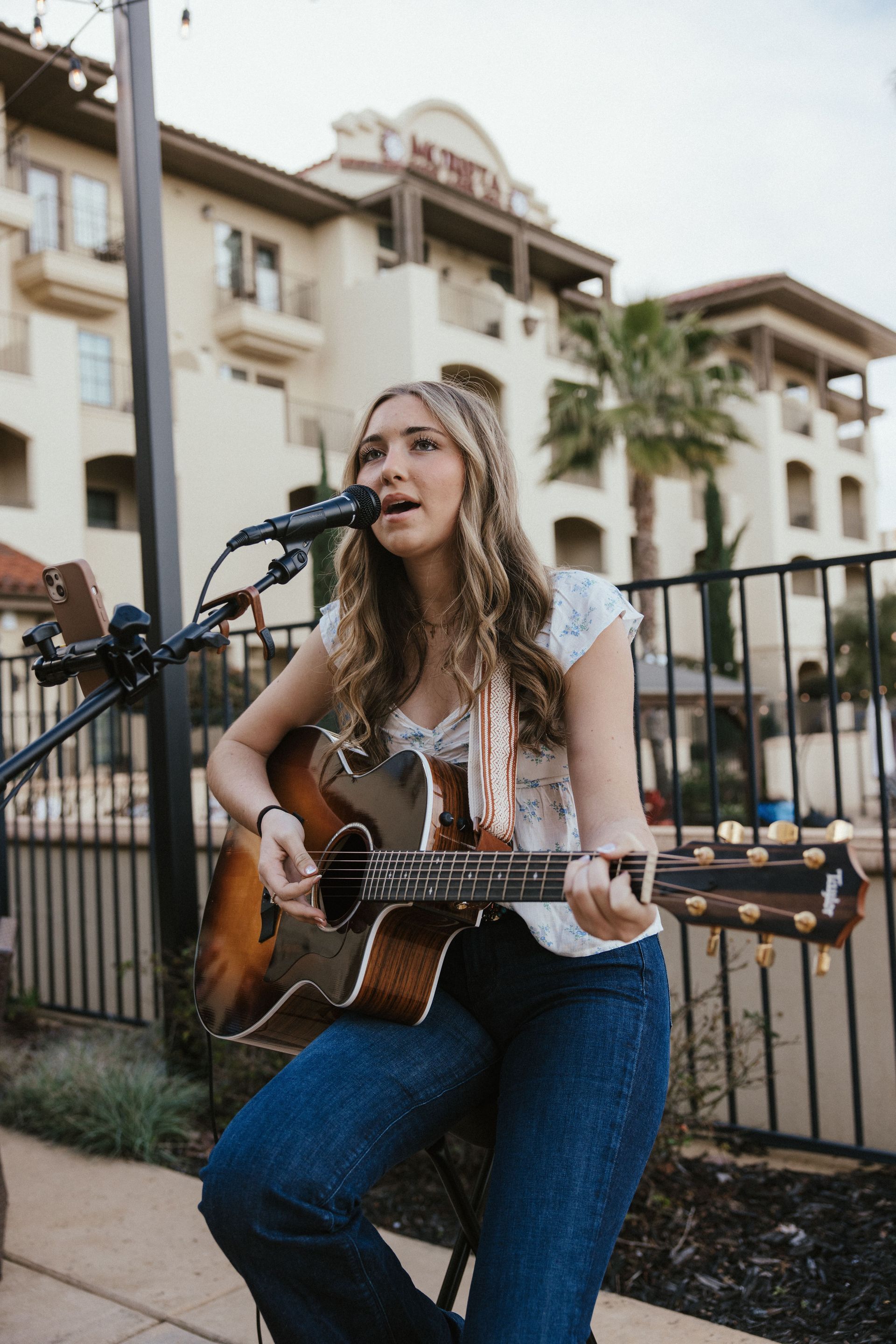 A woman is singing into a microphone while playing an acoustic guitar.