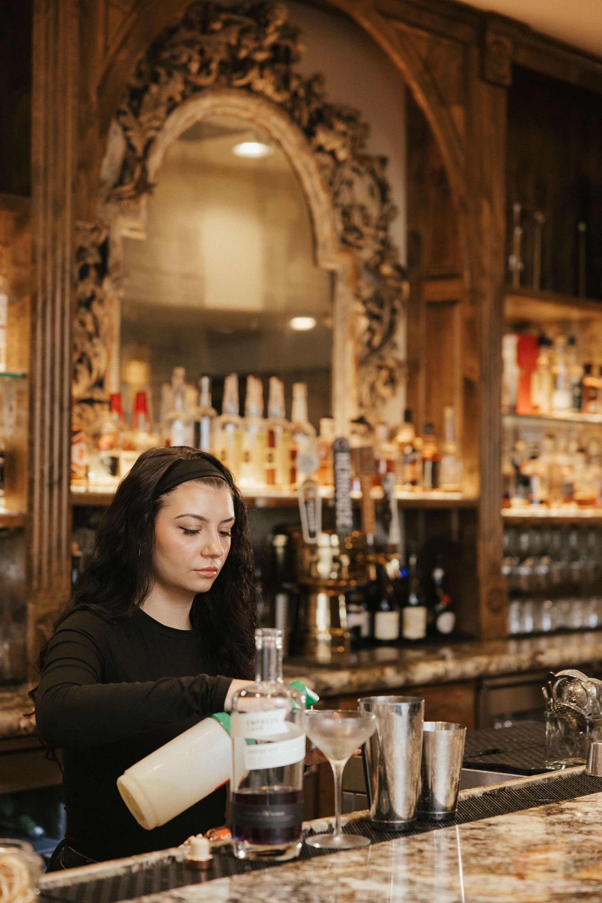 A woman is pouring a drink into a martini glass at a bar.