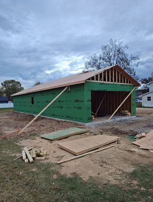 Partially built green house under construction with exposed roof framing and lumber on the ground under a cloudy sky