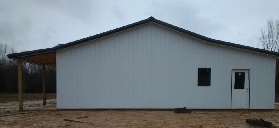 White metal barn with a small porch and two doors on a dirt lot under a gray sky