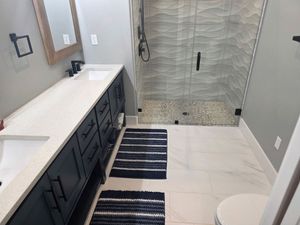 Modern bathroom with double vanity, striped rugs, and a glass walk-in shower