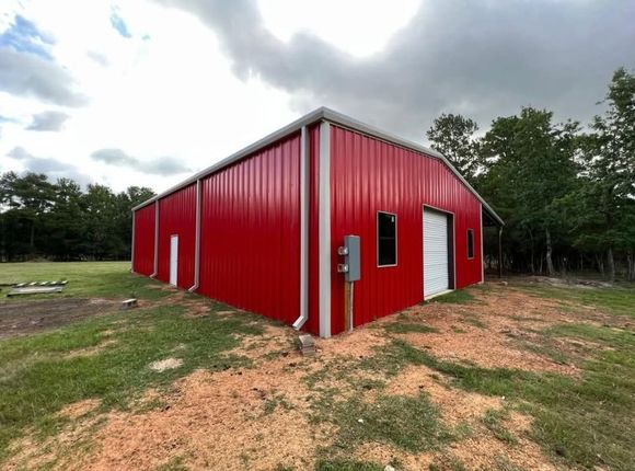 Red metal building with white trim on a grassy lot under cloudy skies