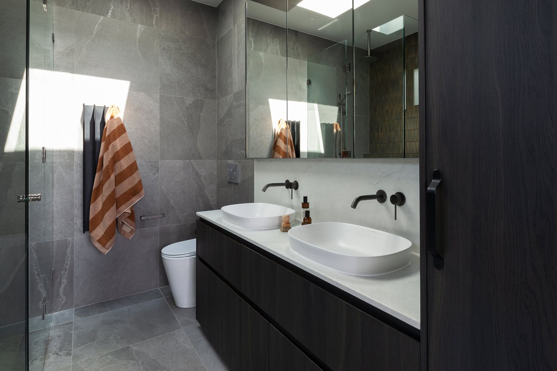 Modern bathroom with double sinks, large mirror, gray tiles, and a striped towel by a glass shower. — Complete Property Projects In Phillip, ACT