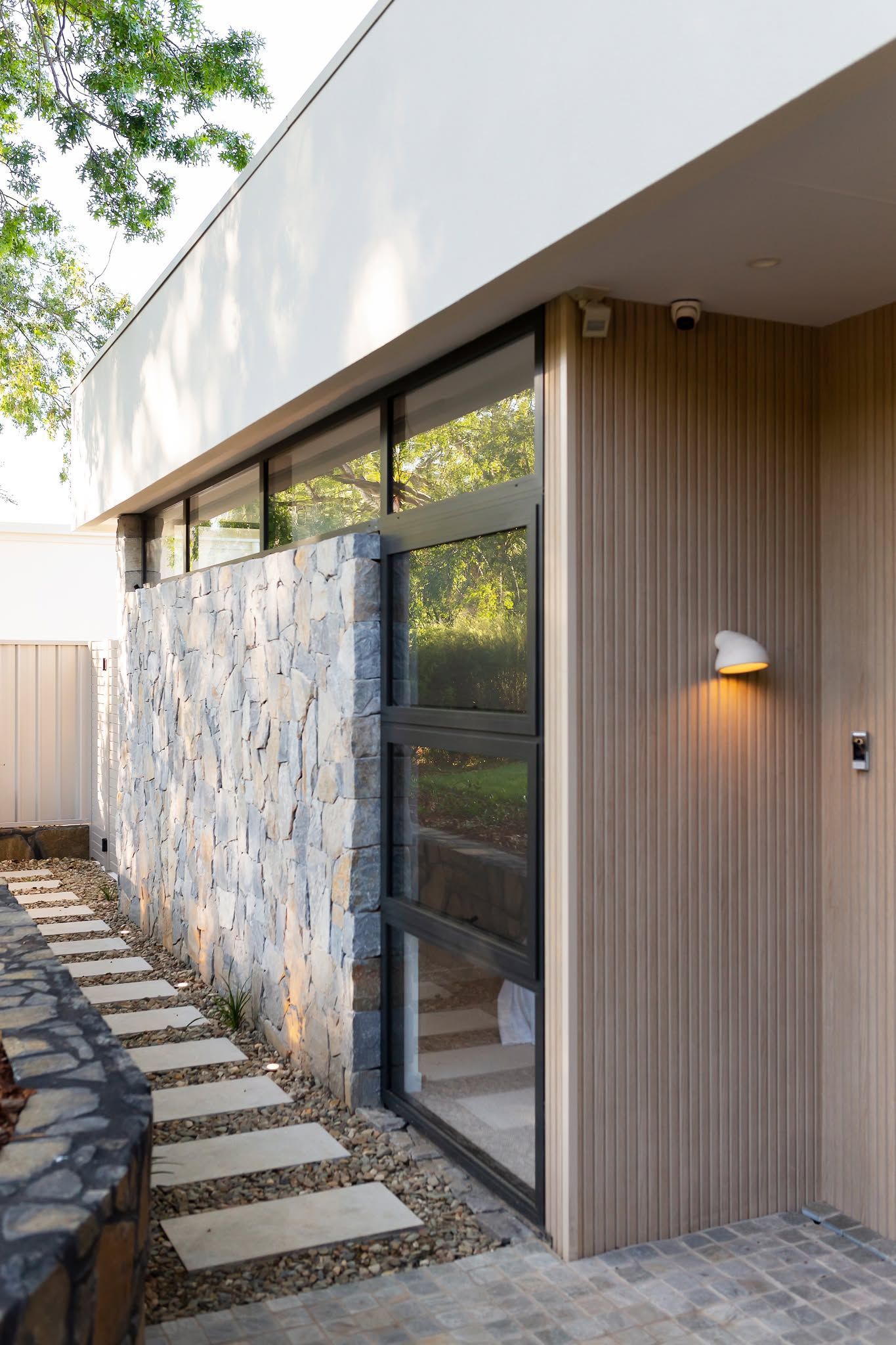 Modern House Exterior with Stone Wall, Wood Siding, Large Windows, and A Stepping-Stone Path — Complete Property Projects In Phillip, ACT