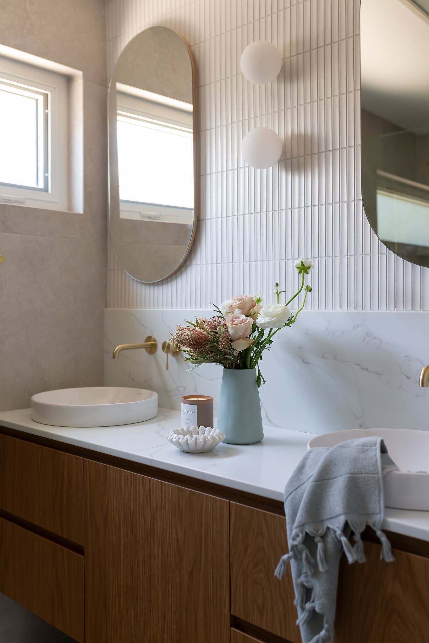 Modern Bathroom Vanity with Oval Mirrors, Wooden Cabinets, White Countertop, and A Vase of Flowers — Complete Property Projects In Phillip, ACT