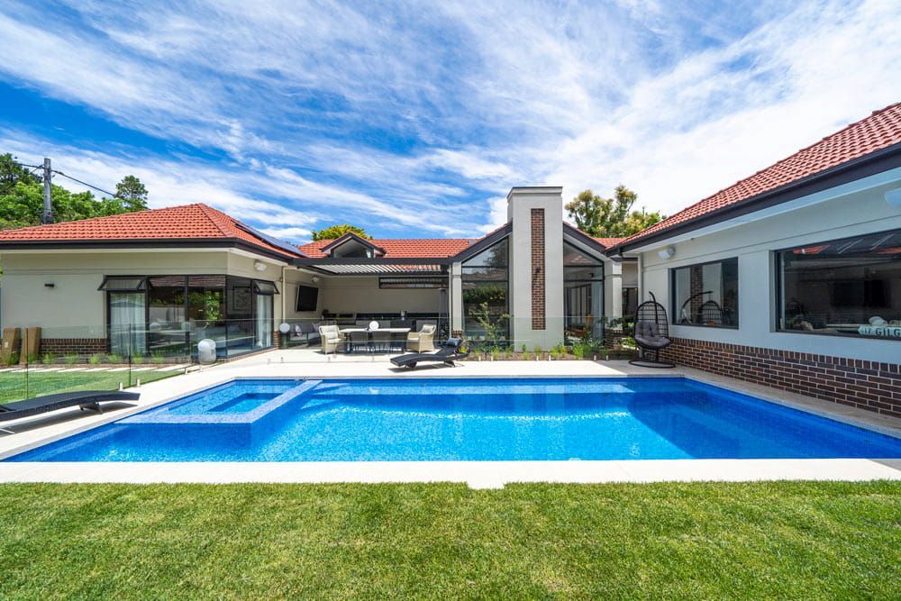 Modern villa with a blue swimming pool, red-tiled roofs, and a sunny backyard under a partly cloudy sky