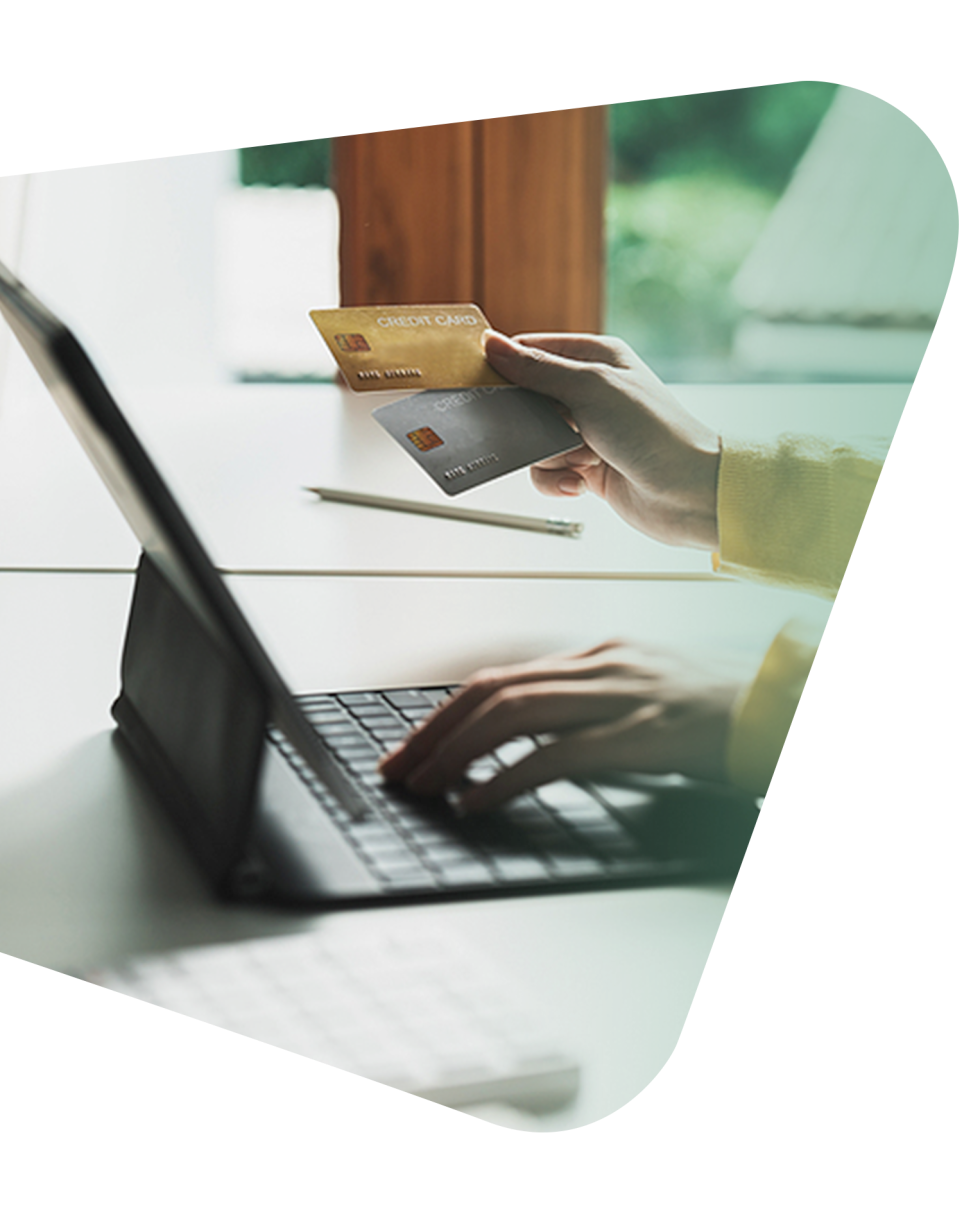 A person in a yellow sleeve types on a laptop while holding a credit card over a desk.