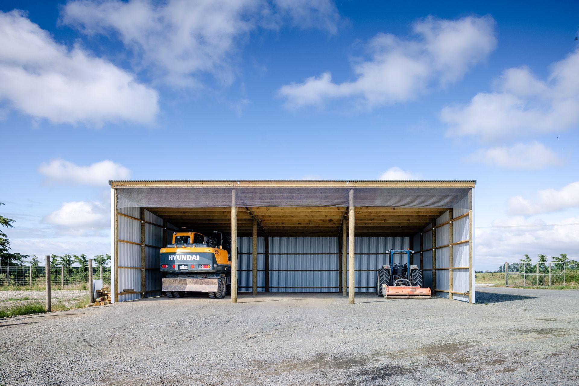 A tractor is parked under a shed on a gravel road.