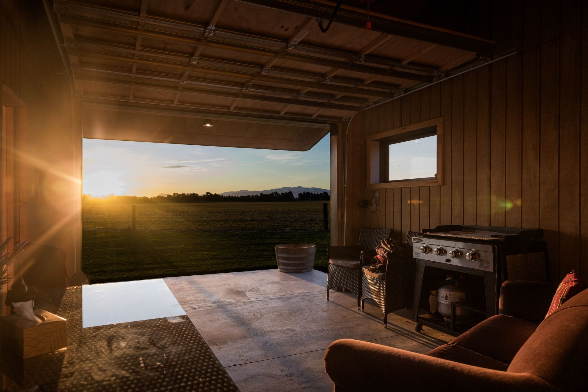 A living room with a chair and a grill with the sun shining through the window.