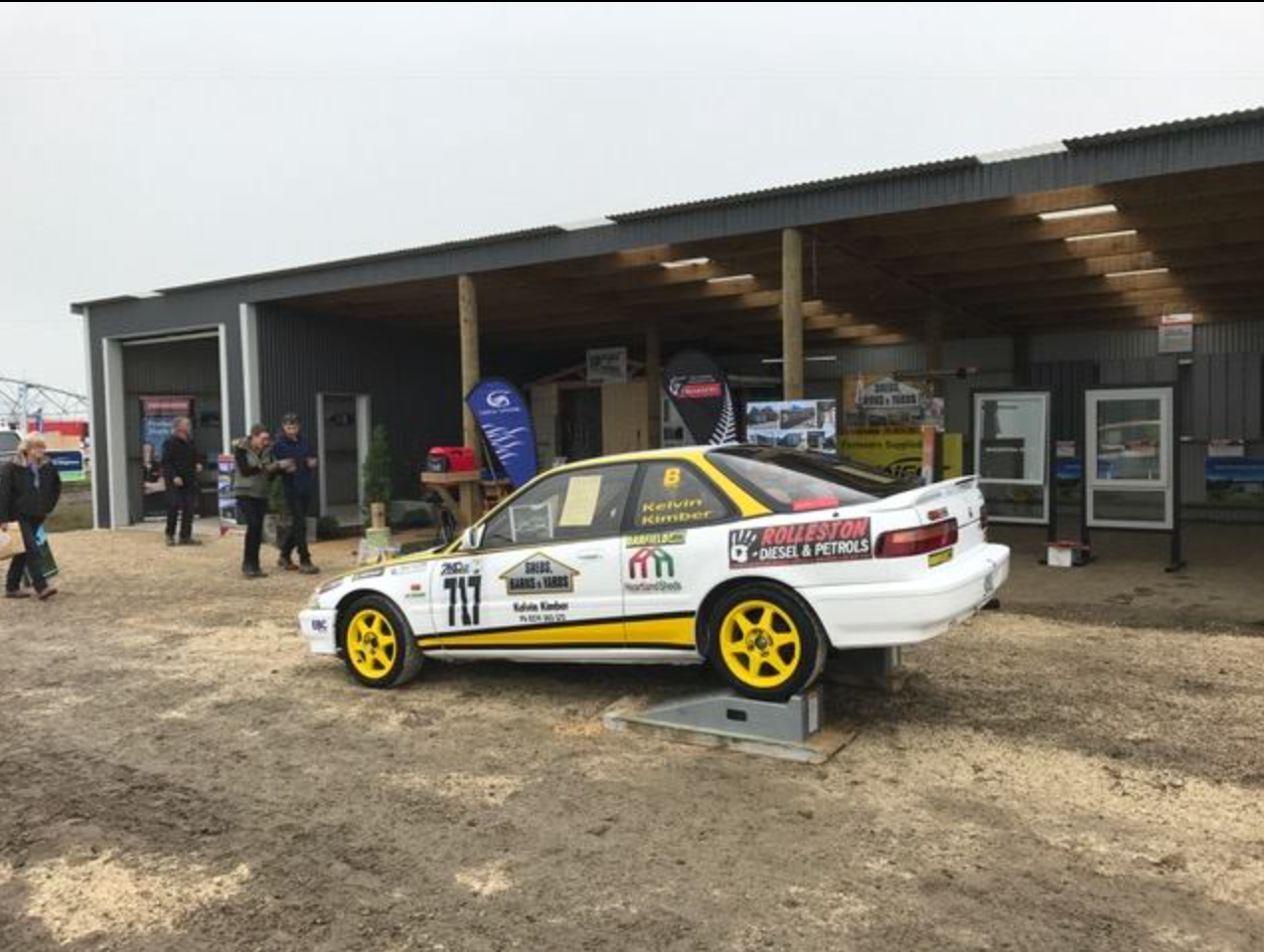 A yellow and white race car is parked in front of a building.