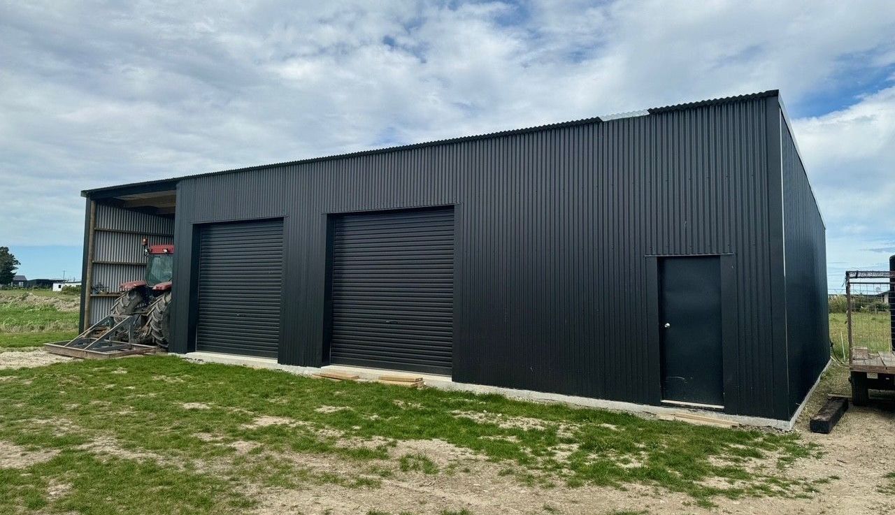A black metal building with two garage doors is sitting in the middle of a grassy field.