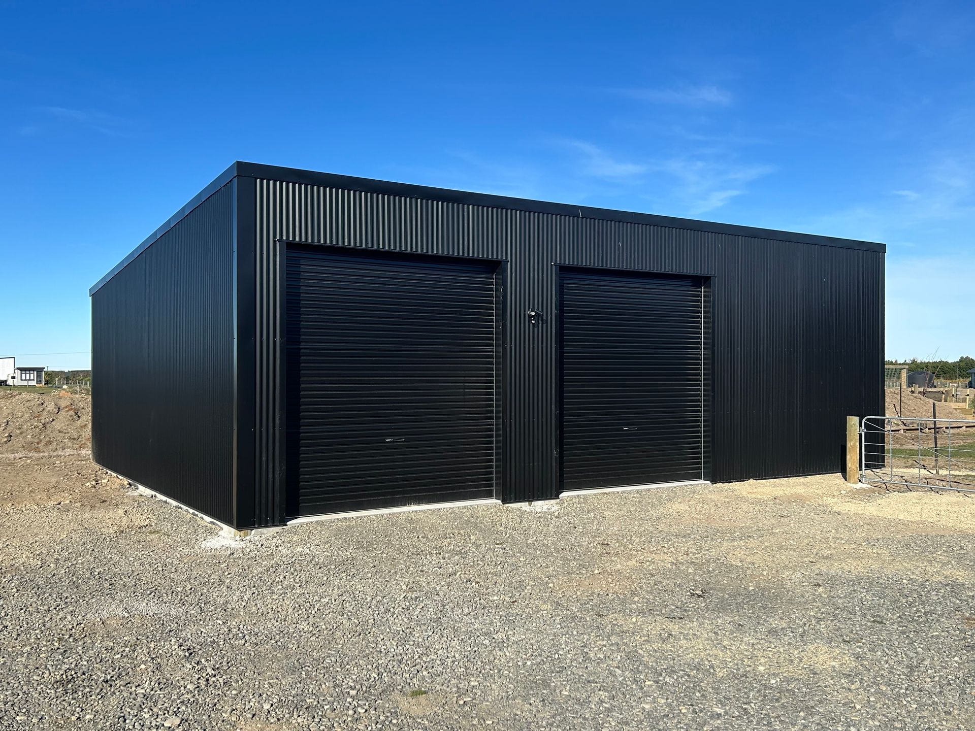 Black corrugated metal garage with two doors, gravel base, and clear blue sky.