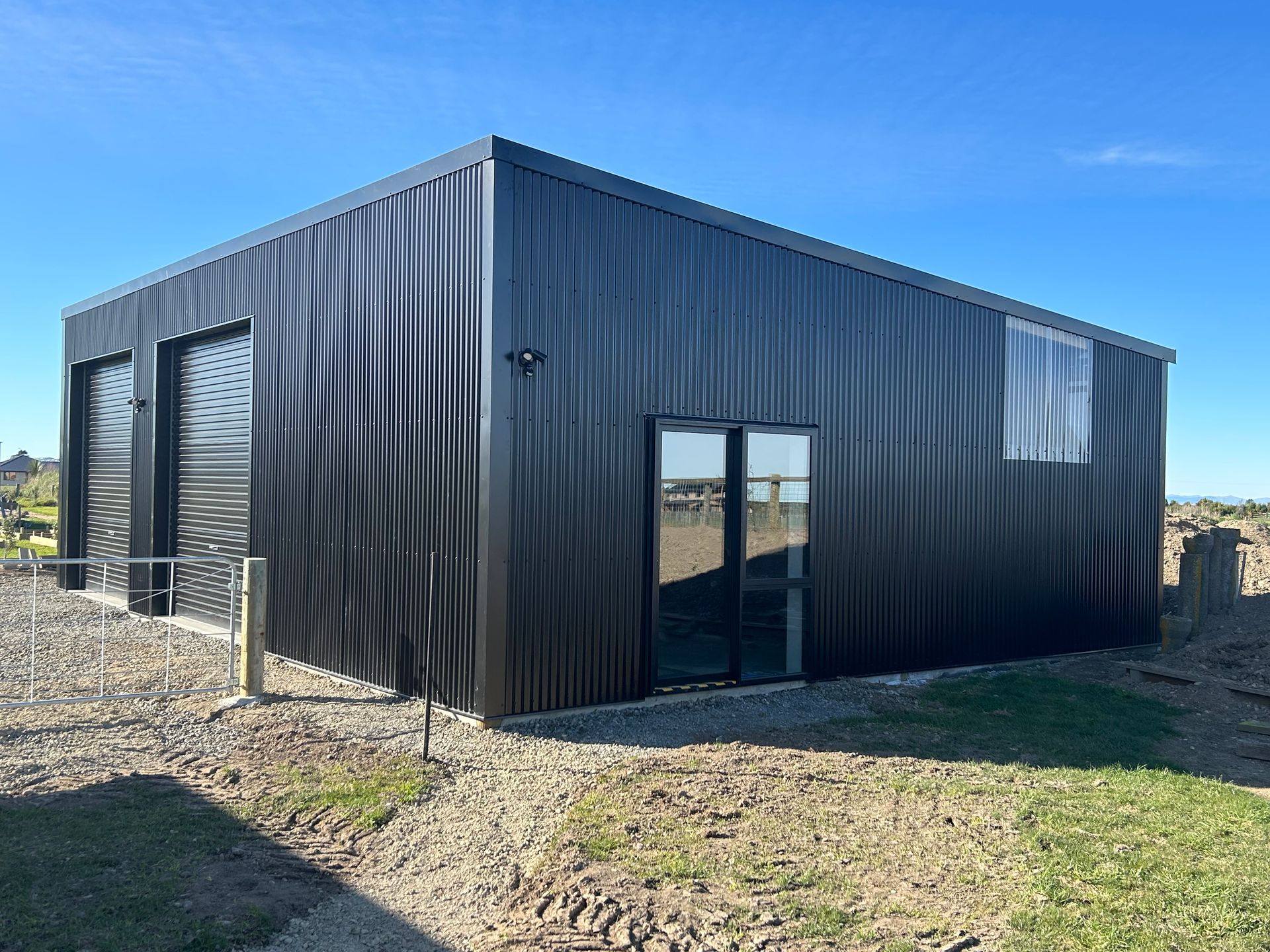 Black corrugated metal building with garage doors, a door, and a window against a blue sky.