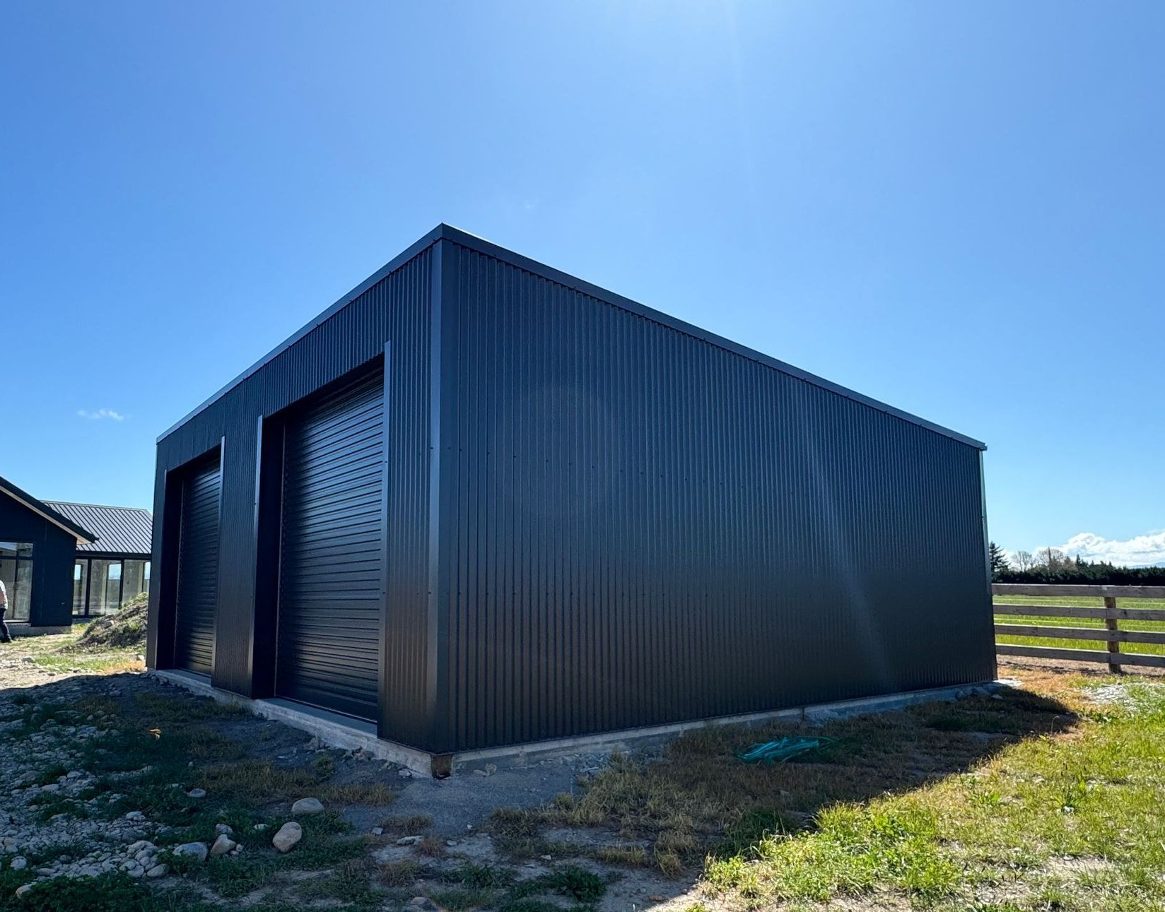 A black garage is sitting in the middle of a grassy field.