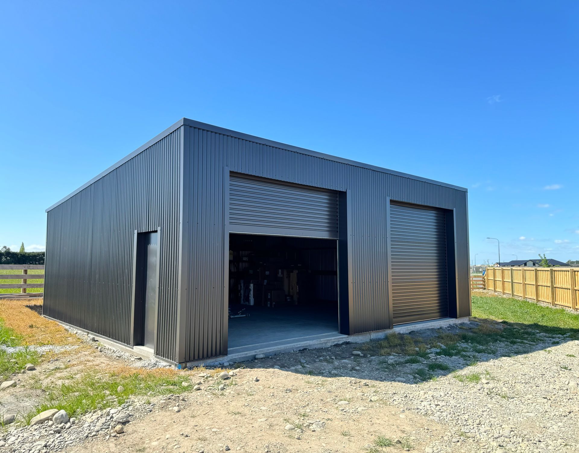 A black garage with two garage doors is sitting on top of a dirt field.