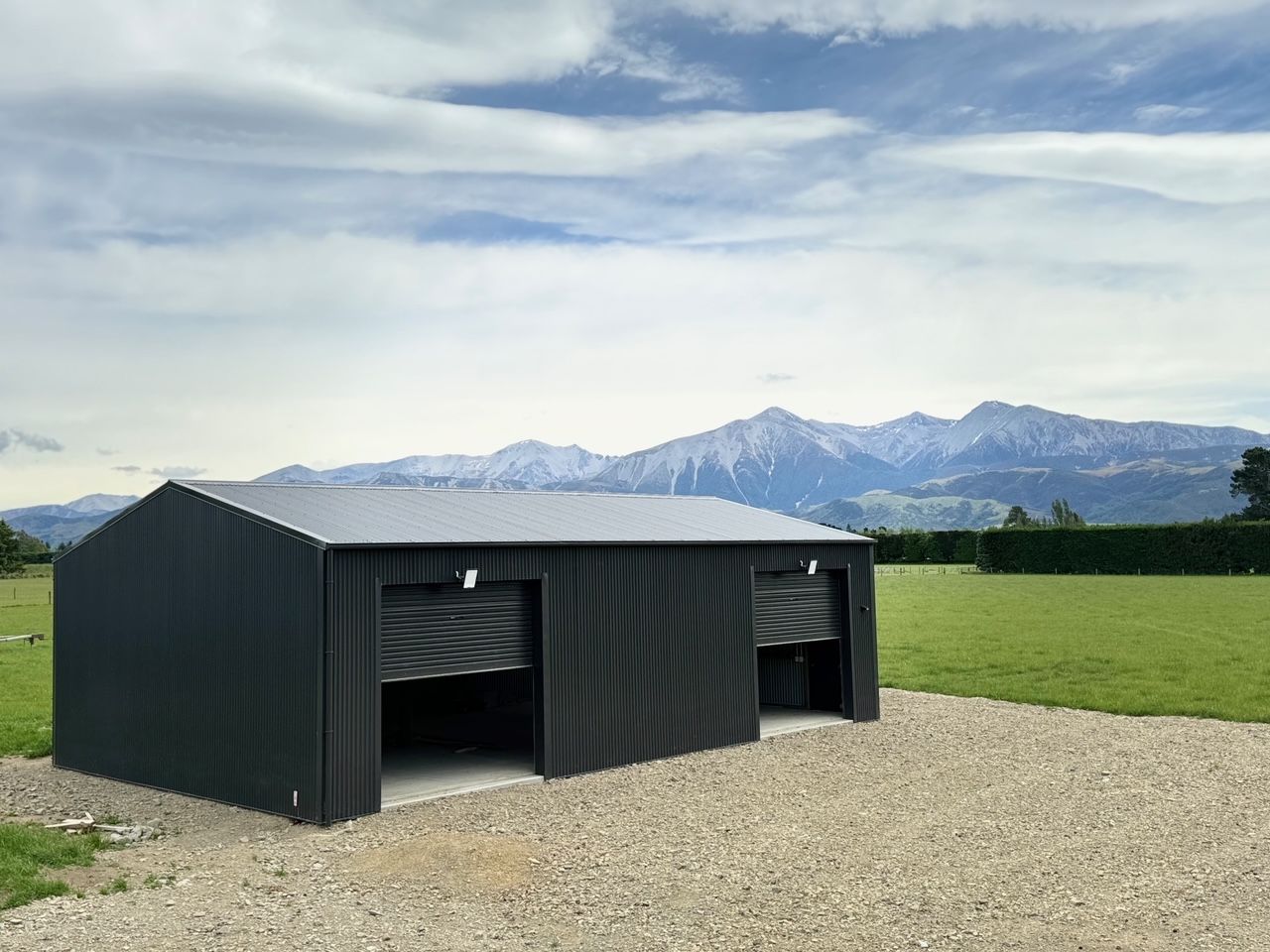 A black garage with mountains in the background is sitting on top of a gravel driveway.