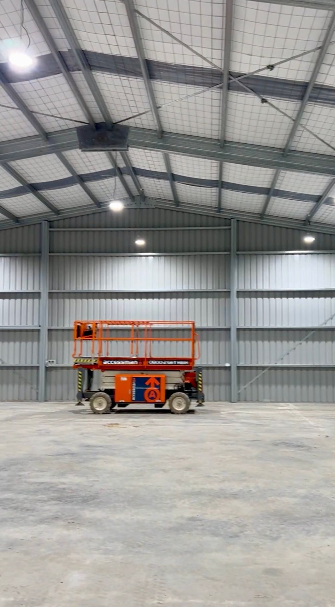 A scissor lift is parked inside of a large warehouse.
